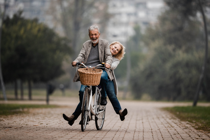 Playful senior couple having fun on a bike in autumn day.